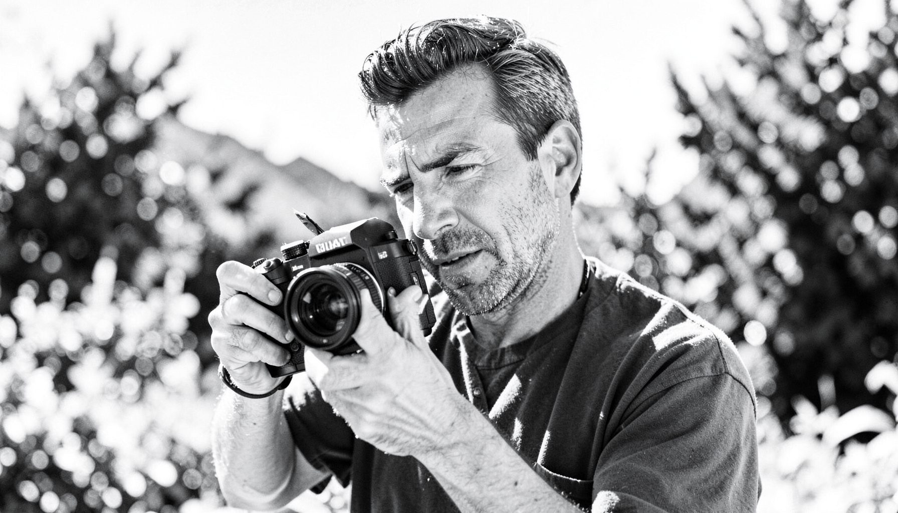 A man holding a film camera in a bright outdoor setting, black and white image with an energetic and creative mood