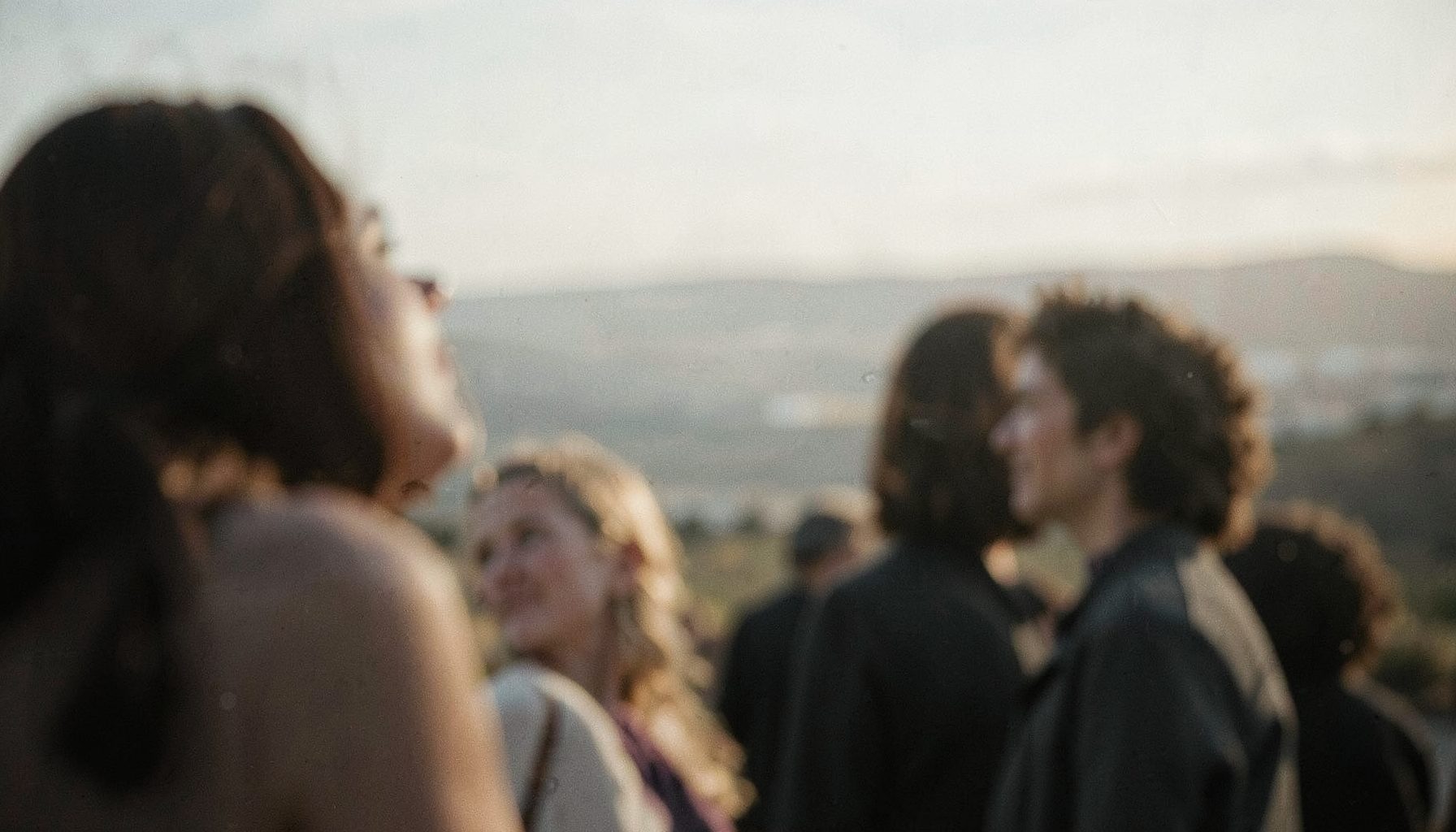 A soft-focus image of people gazing toward a distant horizon, the color palette muted and nostalgic, suggesting longing and the passage of time.