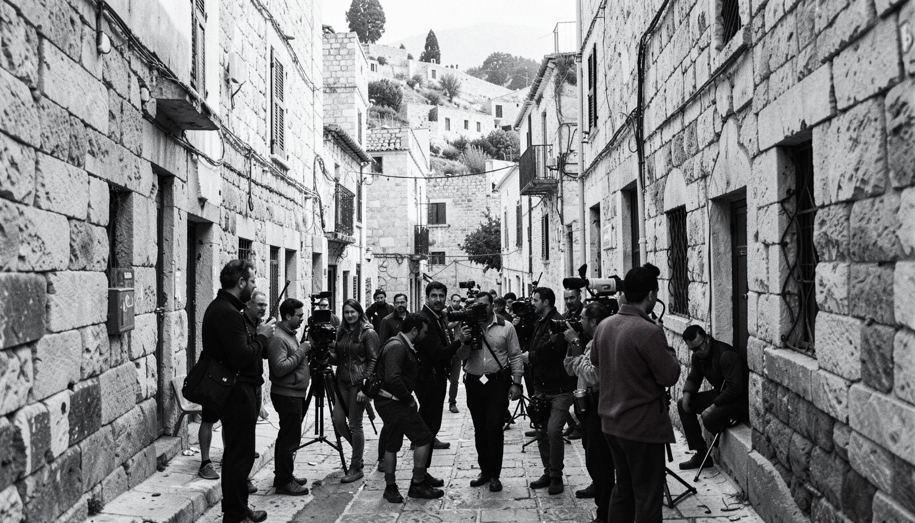 A black-and-white archival photograph of a film crew on location in Jerusalem, with stone buildings and narrow alleyways framing the scene.