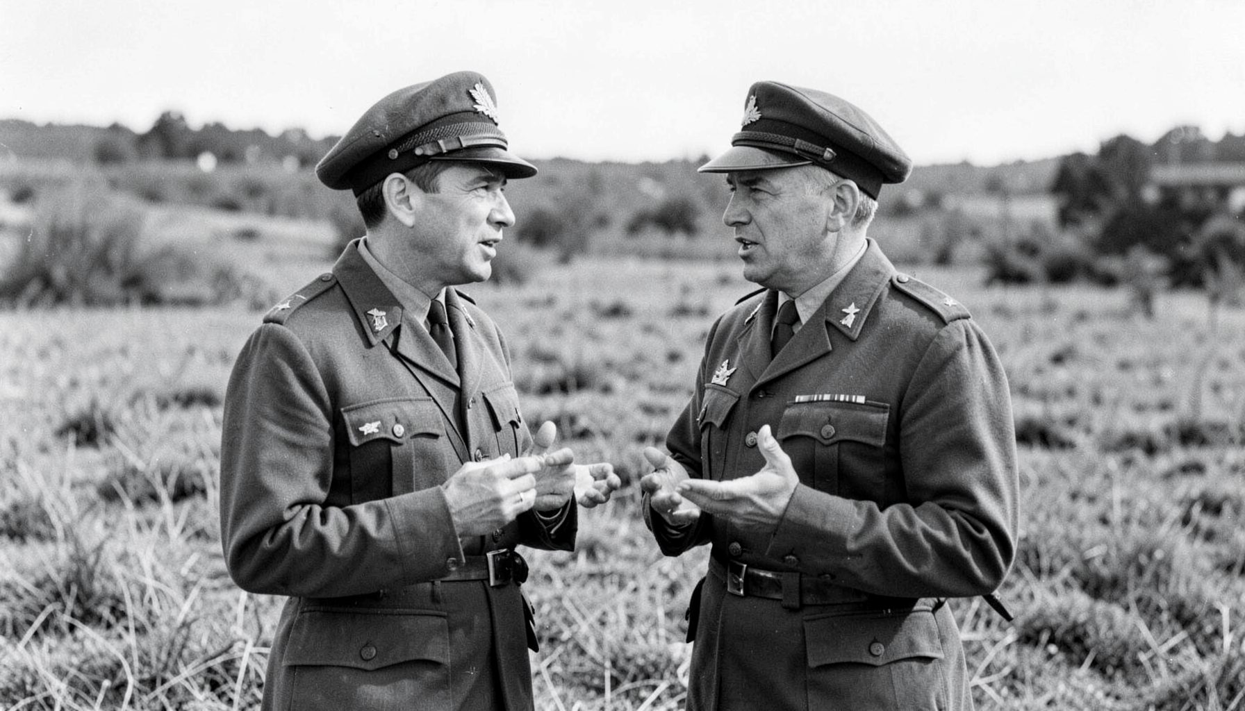Two men in military uniforms speaking in a field, black and white photograph conveying the gravity of wartime reporting